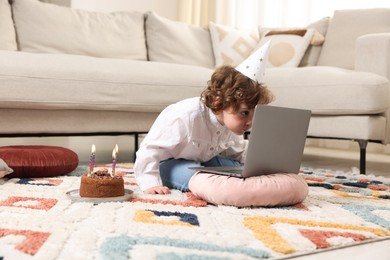 Photo of Birthday celebration. Little boy with cake having video call via laptop at home