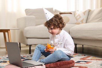 Photo of Birthday celebration. Little boy with cupcake having video call via laptop at home