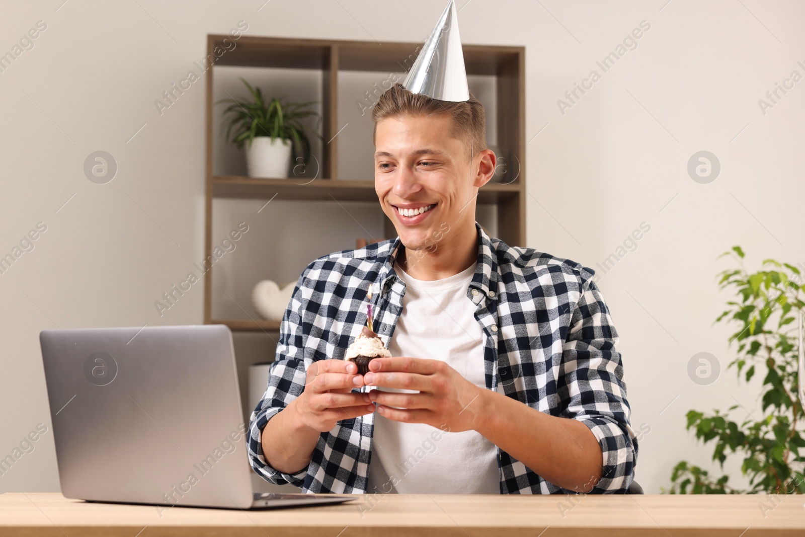 Birthday celebration. Man with cupcake having video call via laptop at table indoors Photo of Birthday celebration. Man with cupcake having video call via laptop at table indoors