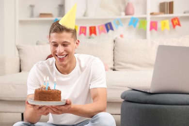 Photo of Man with cake celebrating his birthday and having video call via laptop at home