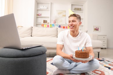 Photo of Man with cake celebrating his birthday and having video call via laptop at home