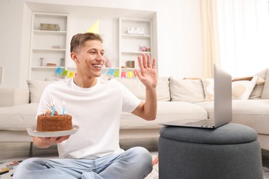 Photo of Man with cake celebrating his birthday and having video call via laptop at home