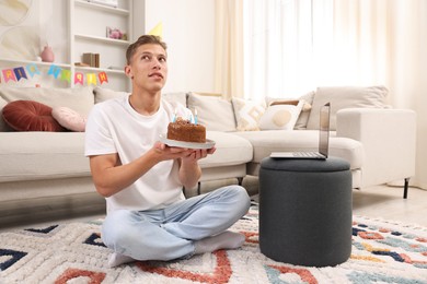 Photo of Birthday celebration. Man with cake making wish while having video call via laptop at home
