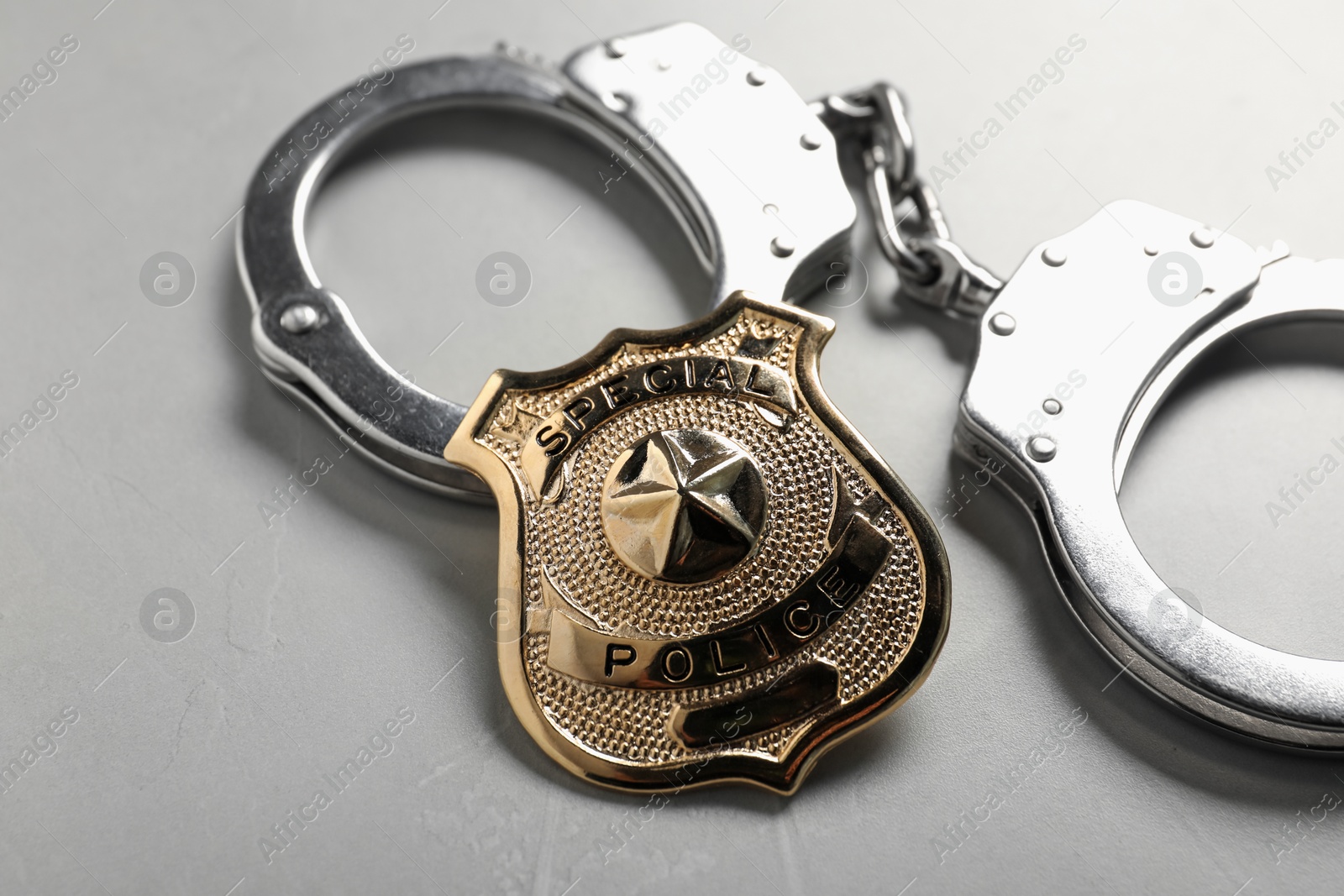 Photo of Police badge and handcuffs on light grey table, closeup