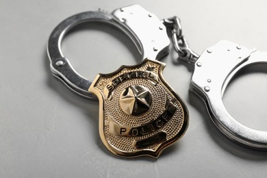 Photo of Police badge and handcuffs on light grey table, closeup