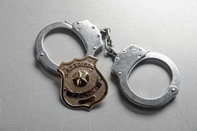 Photo of Police badge and handcuffs on light grey table, above view
