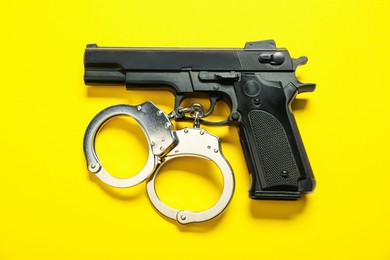 Photo of Black gun and handcuffs on yellow background, flat lay. Police equipment