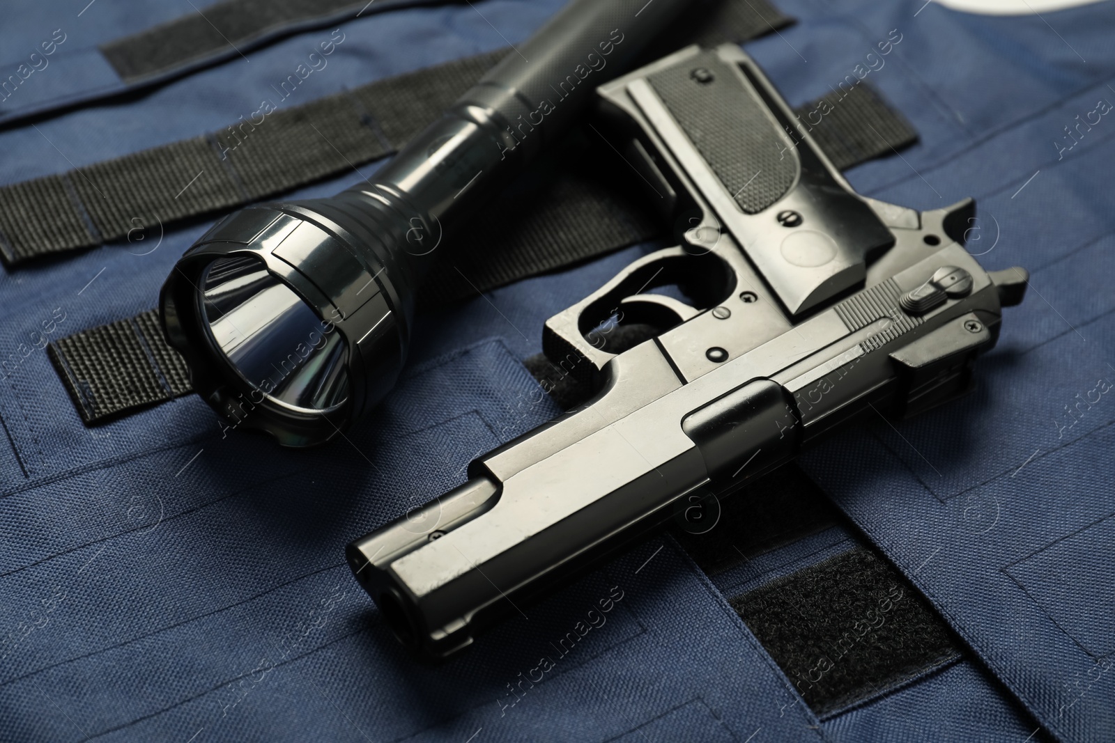 Photo of Flashlight and black gun on bulletproof vest, above view. Police equipment