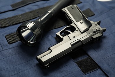 Photo of Flashlight and black gun on bulletproof vest, above view. Police equipment