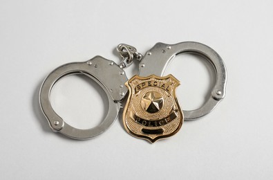 Photo of Police badge and handcuffs on white background, flat lay