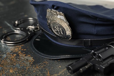 Photo of Police cap, handcuffs and gun on dark table, closeup