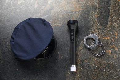 Photo of Police cap, flashlight and handcuffs on dark table, flat lay