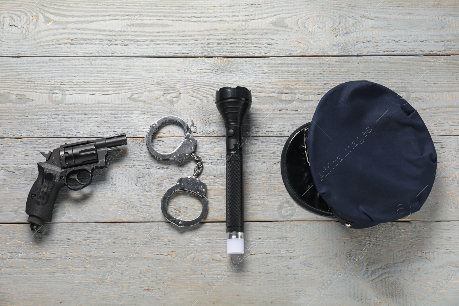 Police cap, flashlight, handcuffs and gun on grey wooden table, flat lay Photo of Police cap, flashlight, handcuffs and gun on grey wooden table, flat lay