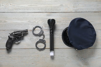 Photo of Police cap, flashlight, handcuffs and gun on grey wooden table, flat lay