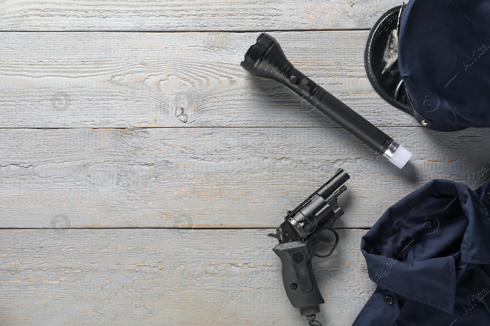 Police uniform, gun and flashlight on grey wooden table, flat lay. Space for text Photo of Police uniform, gun and flashlight on grey wooden table, flat lay. Space for text