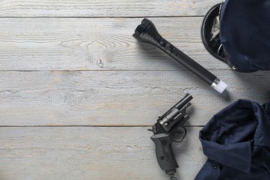 Photo of Police uniform, gun and flashlight on grey wooden table, flat lay. Space for text