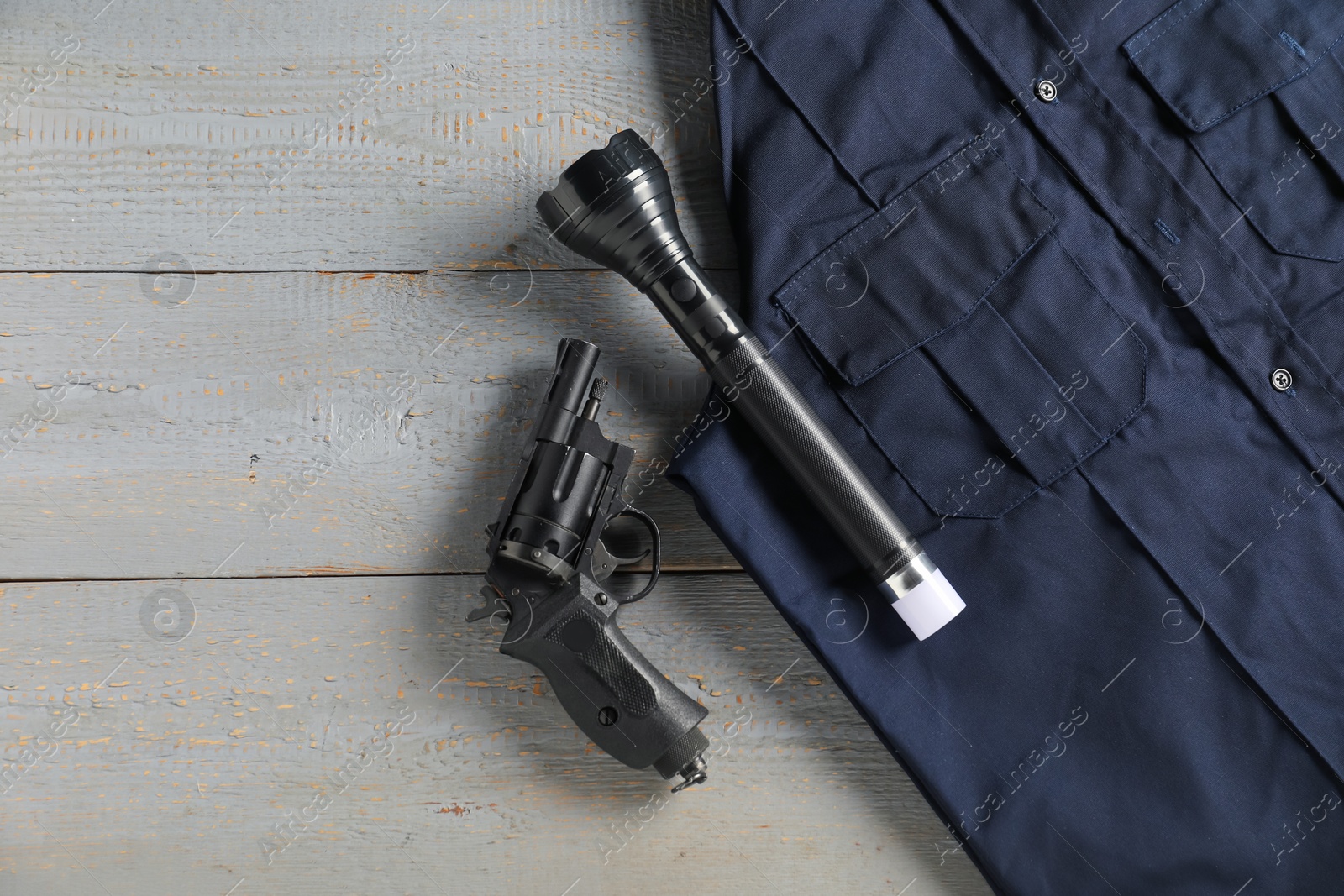 Police uniform, flashlight and gun on grey wooden table, flat lay. Space for text Photo of Police uniform, flashlight and gun on grey wooden table, flat lay. Space for text