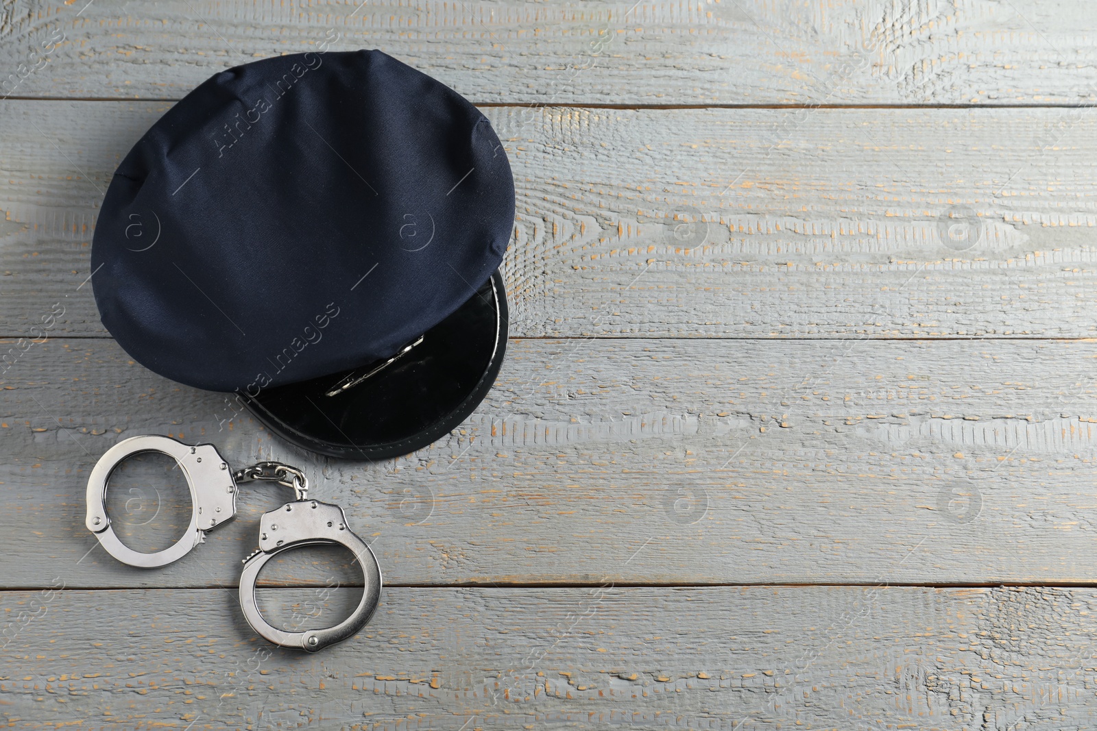 Police cap and handcuffs on grey wooden table, flat lay. Space for text Photo of Police cap and handcuffs on grey wooden table, flat lay. Space for text