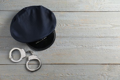 Photo of Police cap and handcuffs on grey wooden table, flat lay. Space for text