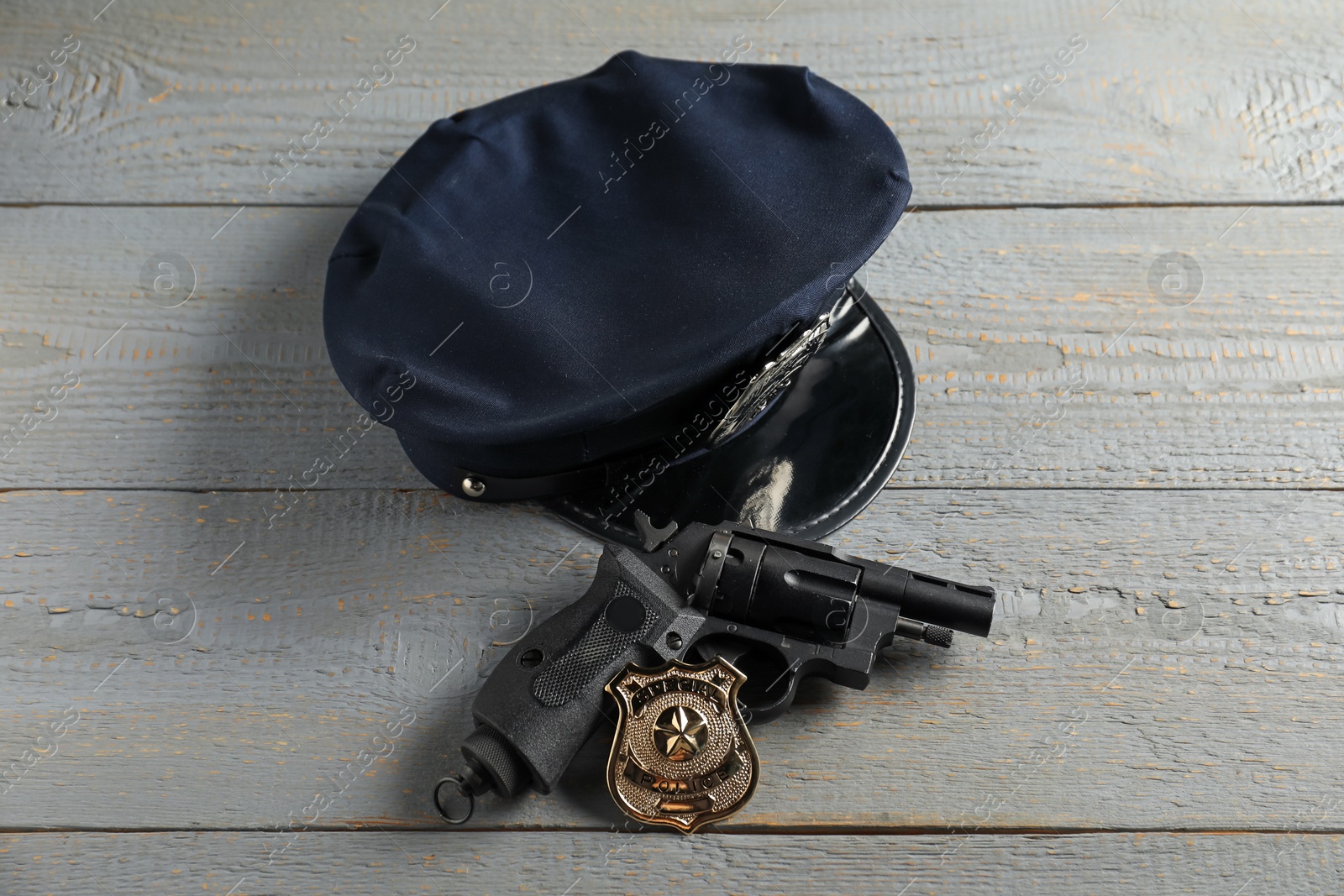 Police cap, gun and badge on grey wooden table, above view Photo of Police cap, gun and badge on grey wooden table, above view