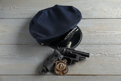 Photo of Police cap, gun and badge on grey wooden table, above view