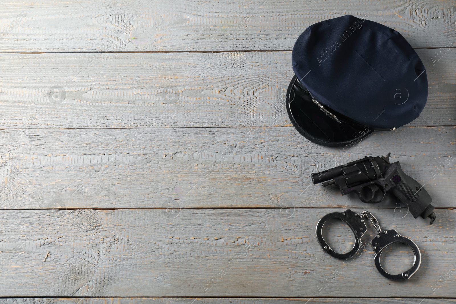 Police cap, gun and handcuffs on grey wooden table, flat lay. Space for text Photo of Police cap, gun and handcuffs on grey wooden table, flat lay. Space for text