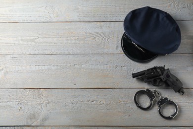 Photo of Police cap, gun and handcuffs on grey wooden table, flat lay. Space for text