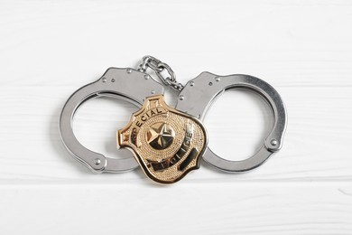 Photo of Police badge and handcuffs on white wooden table, top view