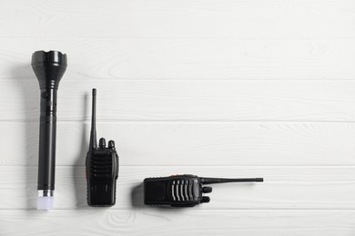 Photo of Police equipment. Flashlight and walkie talkies on white wooden table, flat lay. Space for text
