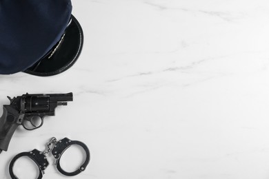 Photo of Police cap, gun and handcuffs on white marble table, flat lay. Space for text