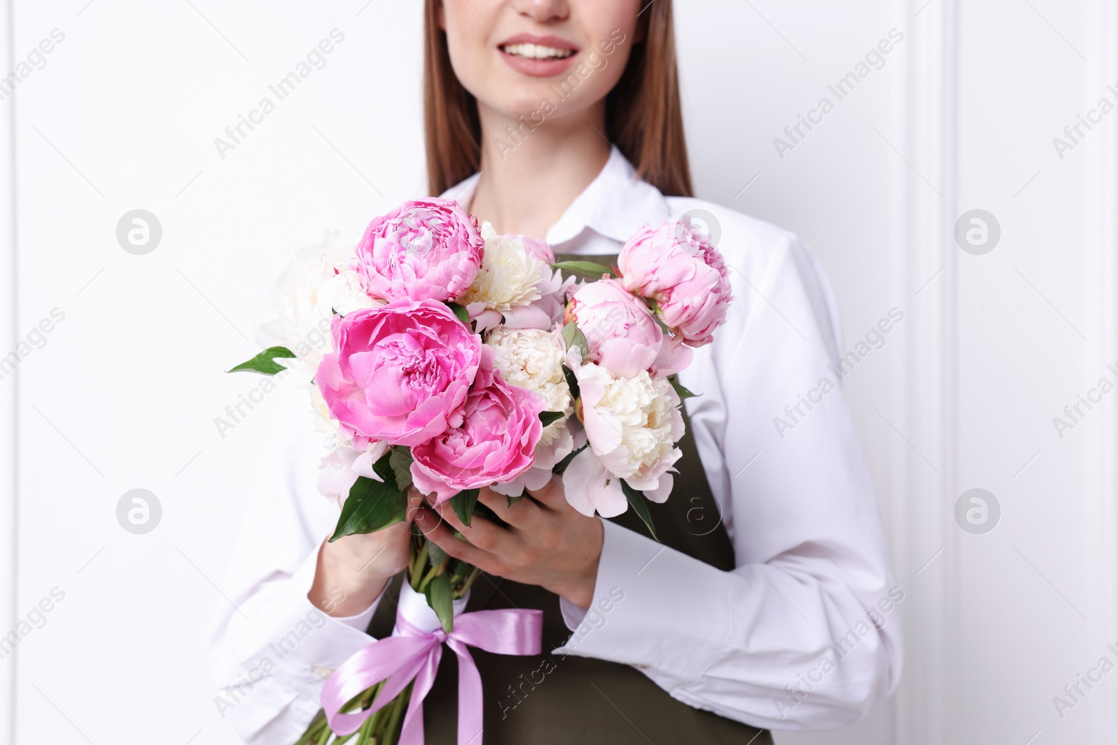 Florist with beautiful bouquet of peonies near white wall indoors, closeup Photo of Florist with beautiful bouquet of peonies near white wall indoors, closeup
