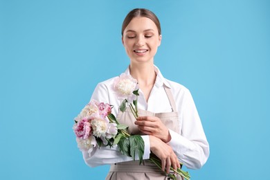 Photo of Florist with beautiful bouquet of peonies on light blue background