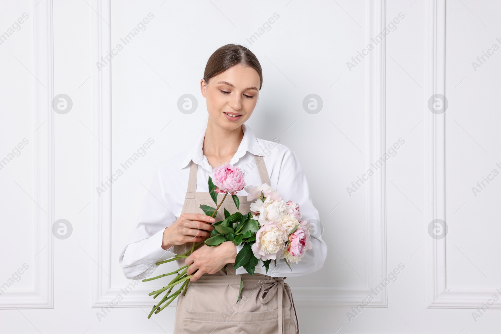 Florist with beautiful bouquet of peonies near white wall indoors Photo of Florist with beautiful bouquet of peonies near white wall indoors