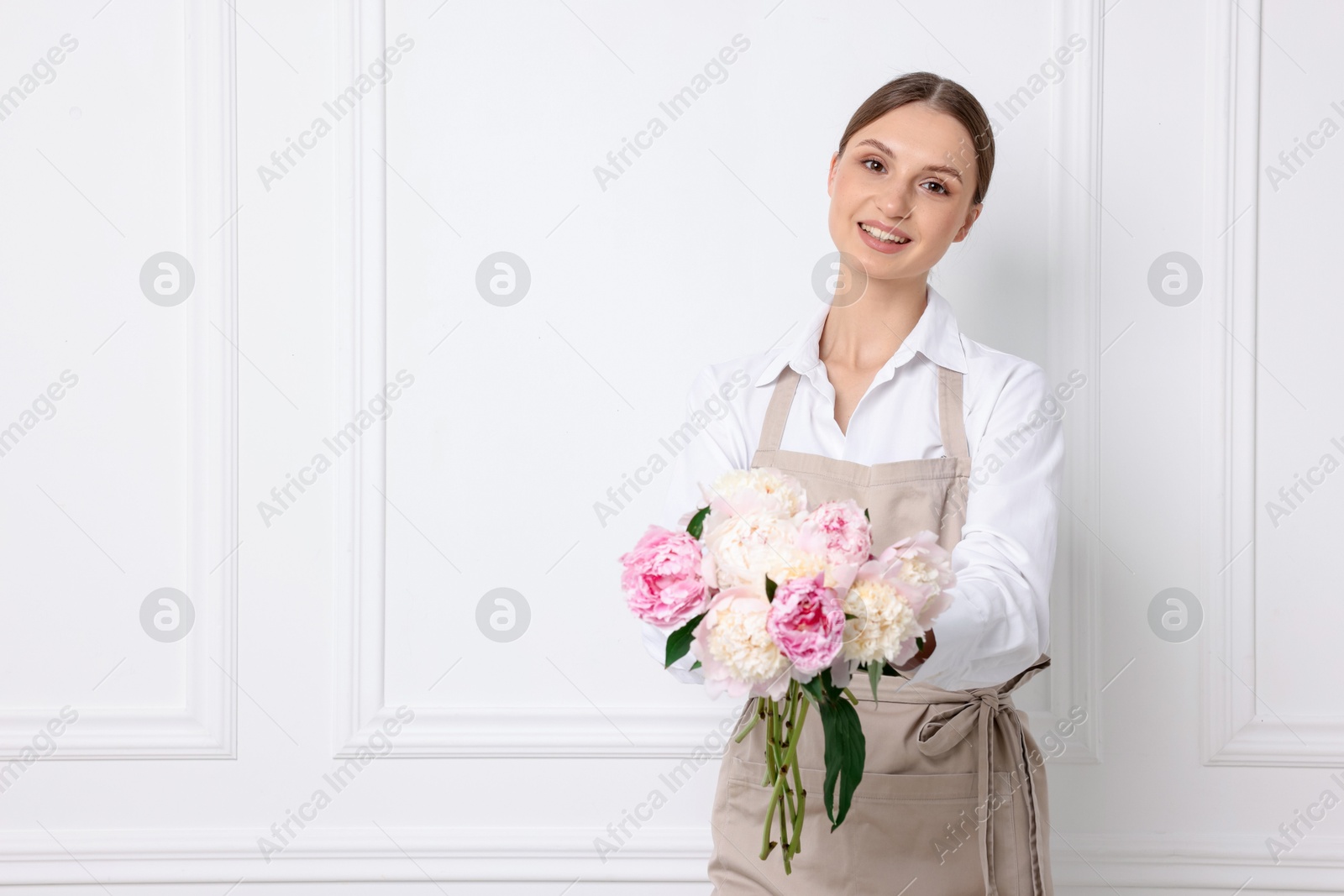Florist with beautiful bouquet of peonies near white wall indoors, space for text Photo of Florist with beautiful bouquet of peonies near white wall indoors, space for text