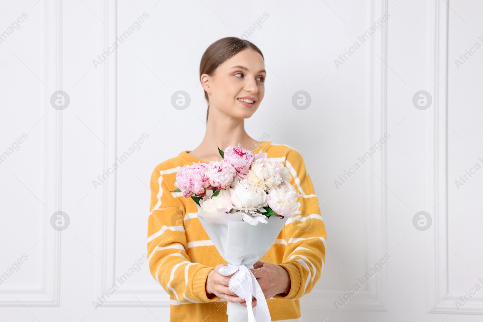 Woman with beautiful bouquet of peonies near white wall indoors Photo of Woman with beautiful bouquet of peonies near white wall indoors