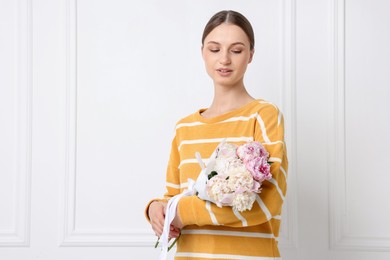 Photo of Woman with beautiful bouquet of peonies near white wall indoors, space for text
