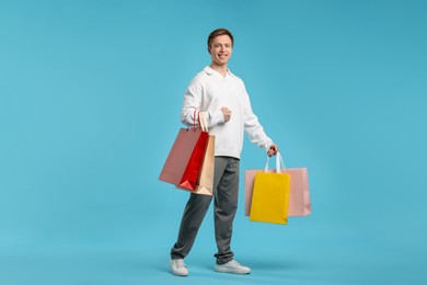Photo of Cheerful man with shopping bags on light blue background