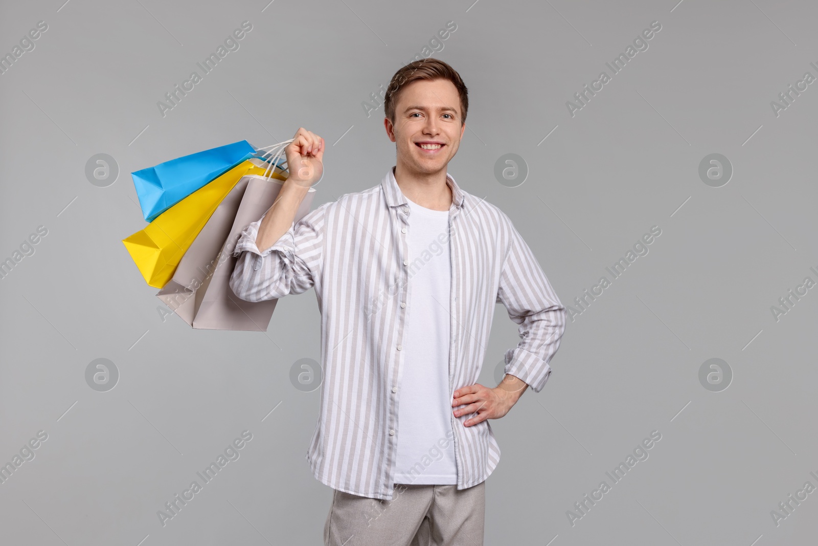 Cheerful man with shopping bags on light grey background Photo of Cheerful man with shopping bags on light grey background