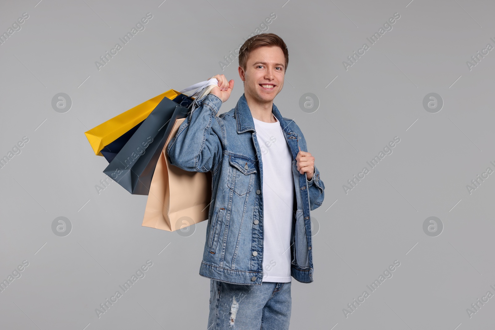 Cheerful man with shopping bags on light grey background Photo of Cheerful man with shopping bags on light grey background