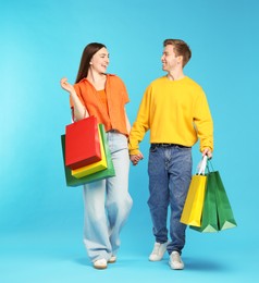 Photo of Happy couple with shopping bags on light blue background