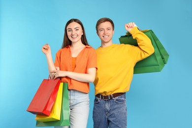 Photo of Happy couple with shopping bags on light blue background