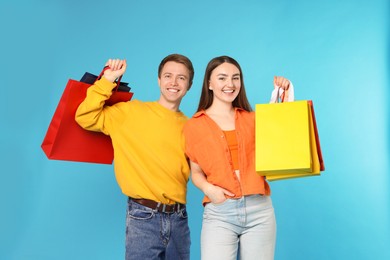 Photo of Happy couple with shopping bags on light blue background