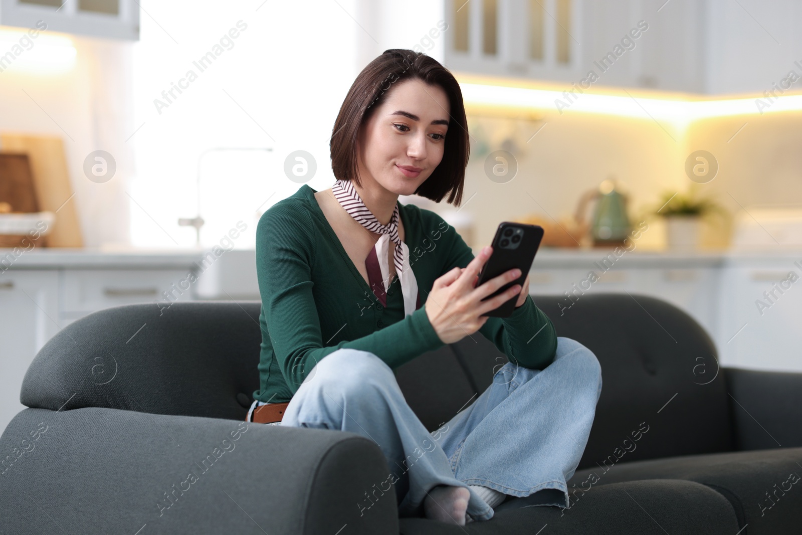 Woman using modern smartphone on sofa at home Photo of Woman using modern smartphone on sofa at home