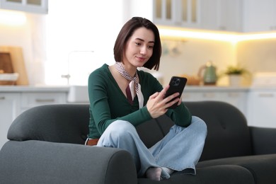 Photo of Woman using modern smartphone on sofa at home