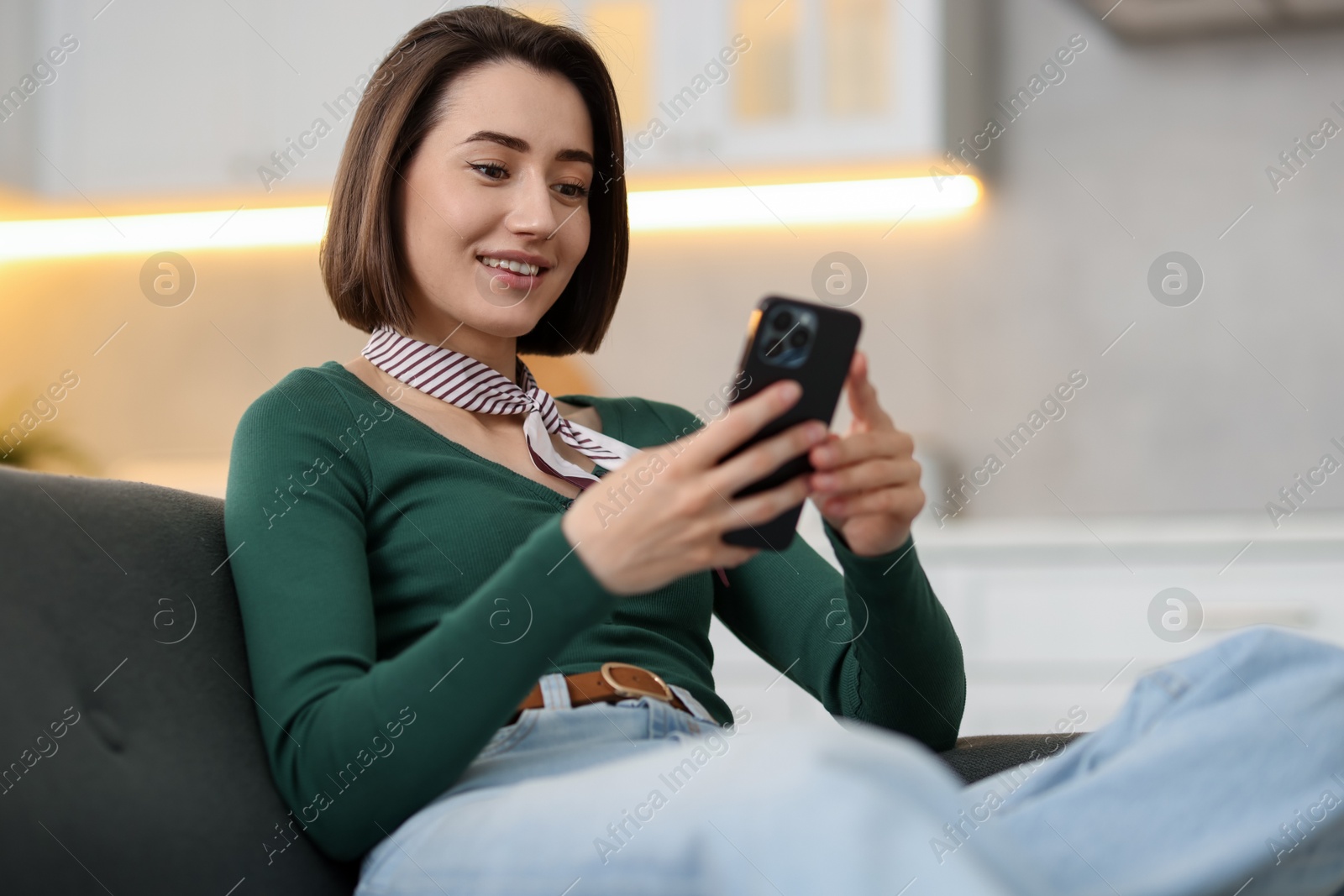 Woman using modern smartphone on sofa at home Photo of Woman using modern smartphone on sofa at home
