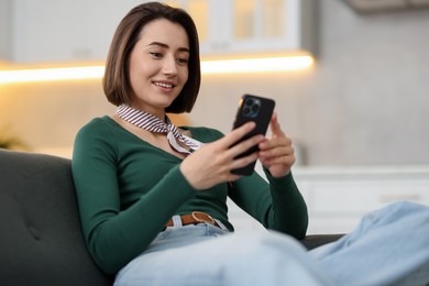 Photo of Woman using modern smartphone on sofa at home