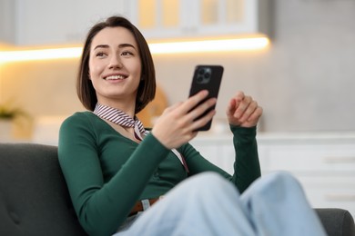 Photo of Woman using modern smartphone on sofa at home
