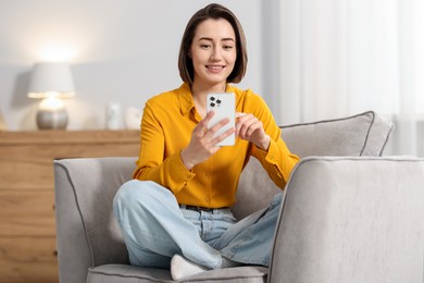 Photo of Woman using modern smartphone in armchair at home
