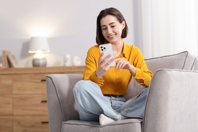 Photo of Woman using modern smartphone in armchair at home