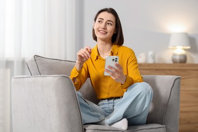 Photo of Woman using modern smartphone in armchair at home